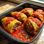 Close-up of homemade cabbage rolls stuffed with meat and rice, simmering in a bright tomato sauce in a baking dish.