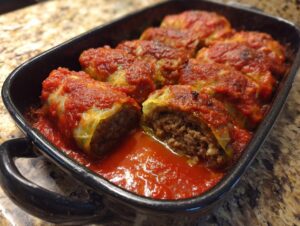 A close-up of baked cabbage rolls smothered in rich tomato sauce in a black baking dish.