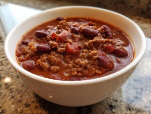 Close-up of a white bowl filled with rich, thick crockpot chili featuring ground meat and kidney beans.