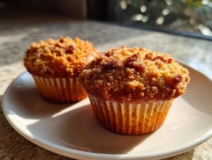 Two freshly baked oatmeal muffins with a generous, crispy crumb topping sitting on a white plate.