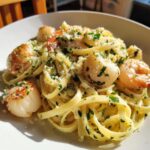 A close-up of creamy fettuccine seafood pasta topped with seared scallops, shrimp, parsley, and grated cheese.