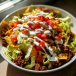 A close-up, appetizing view of a hearty taco salad featuring seasoned ground beef, lettuce, cheese, tomatoes, and sour cream drizzle.