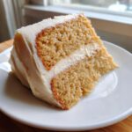 A close-up of a moist slice from the amazing vanilla cake recipe, featuring two layers and thick white frosting.