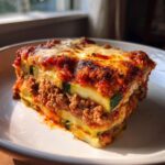 A thick, appetizing slice of zucchini lasagna featuring layers of meat sauce, melted cheese, and zucchini noodles.