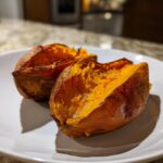 Two halves of perfectly cooked baked sweet potatoes showing fluffy, bright orange insides on a white plate.