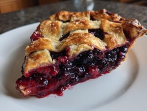 Close-up of a juicy slice of blackberry pie with a golden lattice crust sprinkled with sugar.