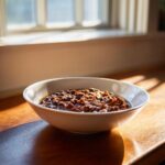 A white bowl filled with rich, savory black eyed peas stewed in a dark sauce, sitting on a wooden surface near a bright window.