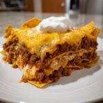 A layered slice of Dorito Casserole featuring seasoned ground beef, melted cheese, and topped with a dollop of sour cream.