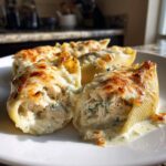 Close-up of baked chicken alfredo stuffed shells overflowing with creamy filling and melted, browned cheese.