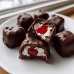 Close-up of homemade chocolate covered cherries, showing the white coconut filling and bright red cherry center.