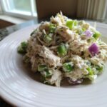 A close-up of a scoop of creamy cottage cheese chicken salad mixed with diced green celery and purple onion on a white plate.