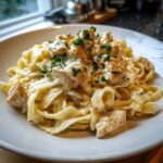 A close-up of a serving of creamy chicken alfredo pasta topped with diced chicken and fresh parsley.