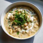 A close-up of creamy white chicken chili topped with sour cream swirls and fresh cilantro.