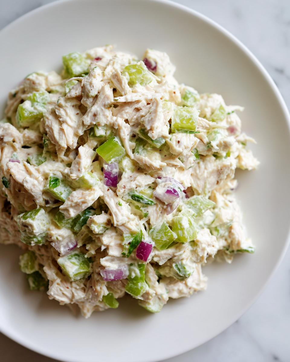 A close-up of creamy cottage cheese chicken salad mixed with chopped celery and red onion served on a white plate.