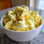 A white bowl filled with creamy, yellow egg salad recipe, generously topped with finely chopped green chives.