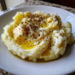 A close-up of fluffy, creamy mashed potatoes topped with melting butter and cracked black pepper.