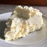 A generous scoop of fluffy, pale yellow protein ice cream served on a white plate.
