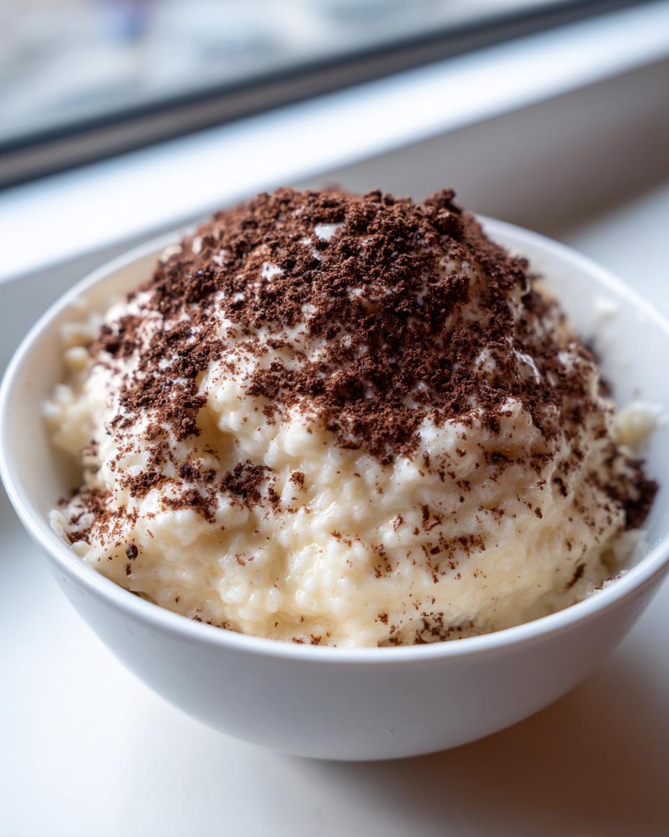 Close-up of creamy rice pudding in a white bowl, generously topped with dark chocolate shavings or cocoa powder.