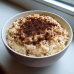 A close-up of creamy rice pudding topped generously with dark cocoa or cinnamon powder in a white bowl.