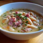 Close-up of a creamy white bean and ham soup, garnished with fresh thyme sprigs.