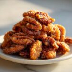 A close-up of a mound of crispy cinnamon sugar pecans coated in sparkling sugar, served on a light plate.
