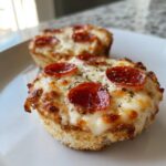 Two freshly baked English muffin pizza halves topped with melted cheese, pepperoni slices, and herbs.