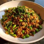 A close-up of a bowl filled with flavorful crispy rice salad mixed with bright green edamame and topped with fresh parsley.