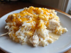 A close-up serving of creamy crock pot chicken and rice topped generously with melted cheddar cheese.