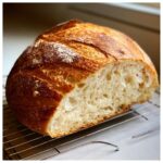 A freshly baked loaf of Italian bread, cut open to show the airy interior crumb, resting on a cooling rack.