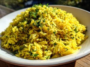 Close-up of fluffy, yellow mediterranean rice seasoned with chopped fresh dill and parsley in a white bowl.
