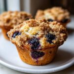 Close-up of a fluffy blueberry muffin topped with brown sugar streusel, showing juicy blueberries.