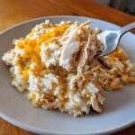 A fork lifting a bite of creamy crock pot chicken and rice topped with melted cheddar cheese.