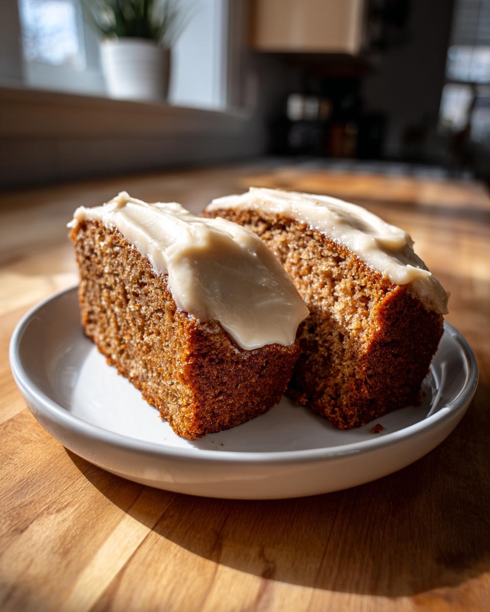 Two moist slices of applesauce cake topped with thick, creamy frosting, served on a white plate.
