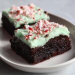 Two fudgy peppermint brownies topped with light green mint frosting and crushed candy canes.