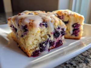 Two moist slices of homemade blueberry scones topped with a thick vanilla glaze, served on a white dish.