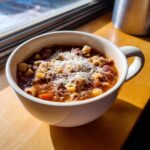 A close-up of a steaming bowl of rich pasta fagioli soup, topped generously with grated Parmesan cheese.