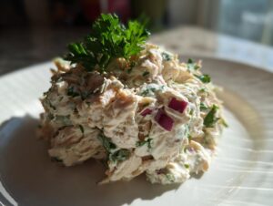 A mound of creamy greek yogurt chicken salad mixed with herbs and red onion, topped with fresh parsley.