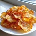 A close-up of a mound of golden brown, homemade potato chips sprinkled with coarse salt.