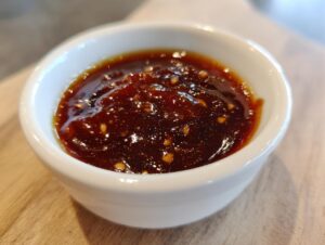 Close-up of thick, glossy homemade teriyaki sauce with visible ginger or garlic bits in a small white dipping bowl.