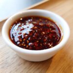 Close-up of thick, glossy homemade teriyaki sauce with visible sesame seeds in a small white dipping bowl.