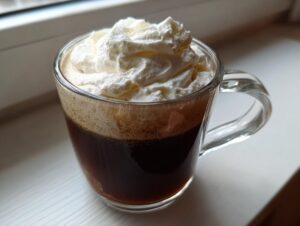 A clear glass mug filled with dark Irish Coffee, topped with a generous layer of whipped cream.