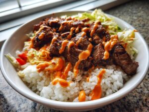 A close-up of a white bowl filled with white rice, topped with sliced Korean BBQ steak and drizzled with spicy orange sauce.