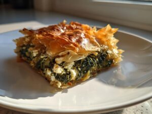 Close-up of a golden, flaky slice of Mediterranean Spinach and Feta Cheese Crisps on a white plate.