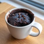 Close-up of a rich, dark chocolate mug cake topped with chocolate chips inside a white mug.