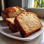 Close-up of a moist slice of sugar free banana bread with a golden crust, served on a white plate.