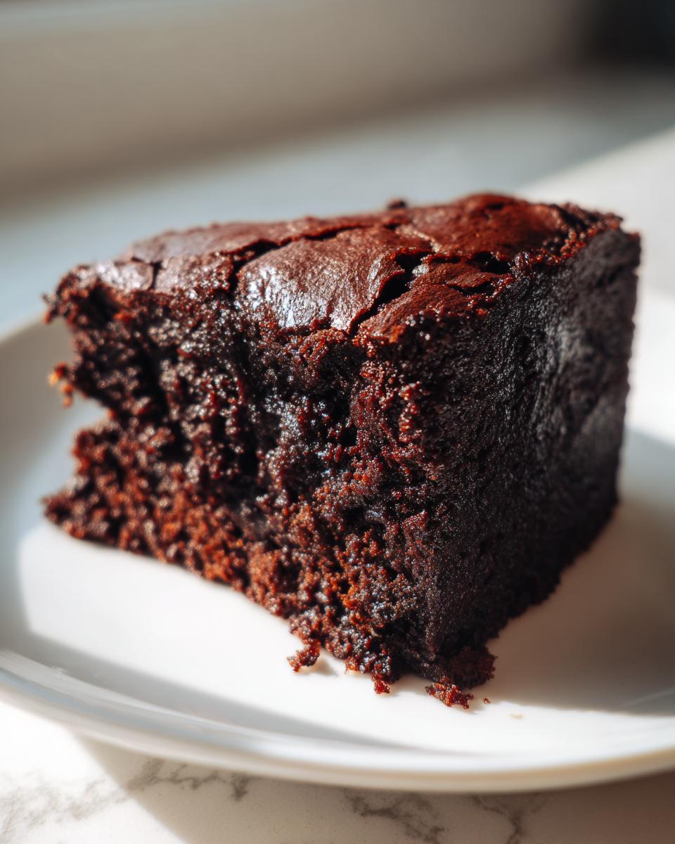 A close-up of a rich, dark chocolate slice of sweet potato brownies on a white plate.