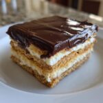 Close-up of a square slice of no bake eclair cake layered with graham crackers, cream filling, and rich chocolate ganache.