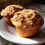 Two freshly baked oatmeal muffins with a thick, crumbly cinnamon streusel topping resting on a white plate.