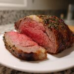 Close-up of a medium-rare prime rib recipe roast, sliced to show the juicy pink center and herb crust.
