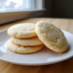 A stack of four perfectly shaped, lightly golden sugar cookie rounds sprinkled with granulated sugar.